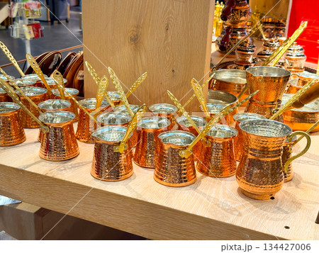 Turkish Copper cezve coffee pots arranged on wooden shelf in souvenir shop. Traditional coffee preparation, metal craftsmanship, cultural ritual, hospitality heritage, artisanal cookware and retail 134427006