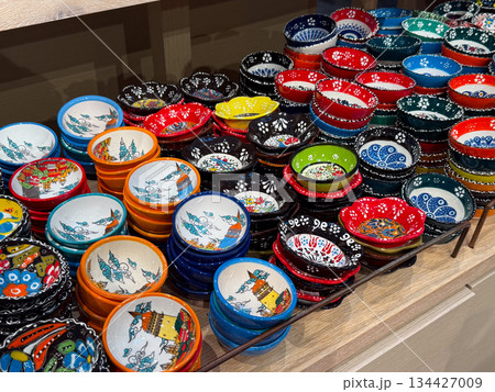 Colorful handmade ceramic Turkish bowls arranged on wooden shelves. Tableware variety, functional art, culinary culture, artisan production, household tradition, decorative ceramics and retail 134427009
