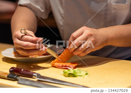 Skilled chef slicing fresh salmon with precision in a modern kitchen Skilled chef slicing fresh salmon with precision in a modern kitchen 134427029