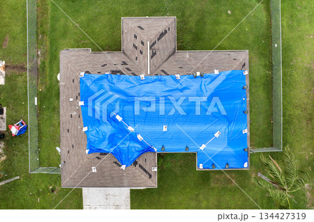 Home rooftop wrapped in plastic tarp following hurricane damage, protecting structure from water penetration until permanent roofing materials are restored Home rooftop wrapped in plastic tarp following hurricane damage, protecting structure from water penetration until permanent roofing materials are restored 134427319