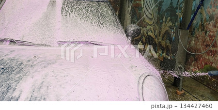 Car wash with pink foam covering vehicle in vibrant outdoor setting 134427460