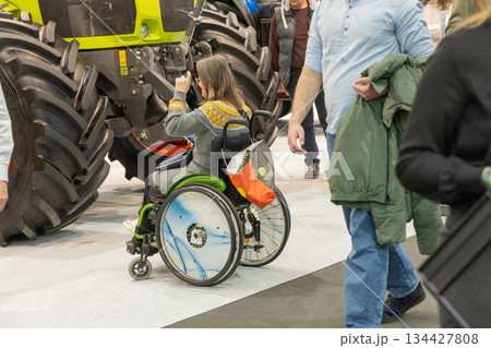 Berlin, Germany - January 21, 2025: Woman in wheelchair photographing tractor at expo Berlin, Germany - January 21, 2025: Woman in wheelchair photographing tractor at expo 134427808