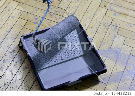 A paint roller and tray filled with gray paint rest on a herringbone wooden floor 134428212
