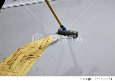 Renovating a parquet floor with gray paint using a paint roller: Highlighting worker's Renovating a parquet floor with gray paint using a paint roller: Highlighting worker's 134428214