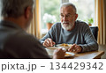 Two elderly men enjoying a meal together in a cozy dining room during a sunny afternoon 134429342