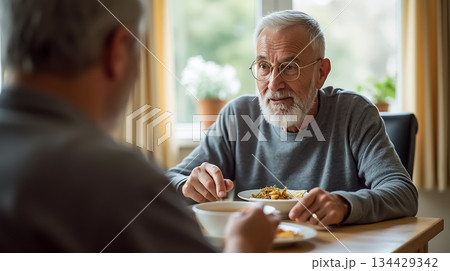 Two elderly men enjoying a meal together in a cozy dining room during a sunny afternoon 134429342