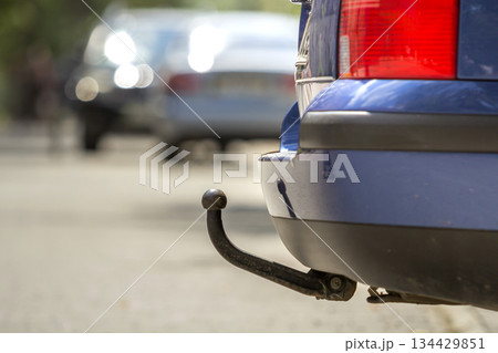 Blue car parked on sunny street, red stop lights, hook for dragging trailer, tow hitch or towbar. 134429851