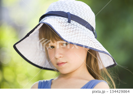 Close-up portrait of serious little girl in a big hat. Child having fun time outdoors in summer. Close-up portrait of serious little girl in a big hat. Child having fun time outdoors in summer. 134429864