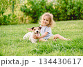 Happy small girl hugging jack russell terrier dog on green grass lawn - child pet friendship 134430617