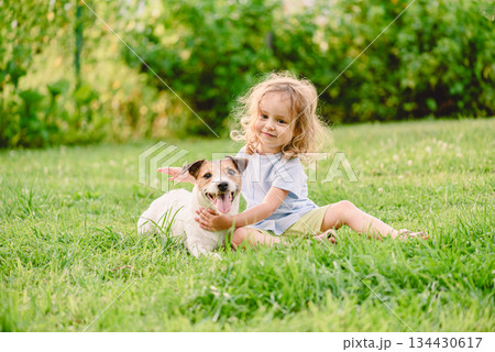 Happy small girl hugging jack russell terrier dog on green grass lawn - child pet friendship Happy small girl hugging jack russell terrier dog on green grass lawn - child pet friendship 134430617