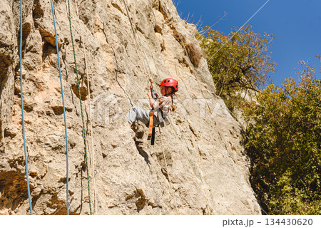 Child rock climbing training with safety equipment on natural rock wall. Snappelling (Rappelling) in Israel. 134430620