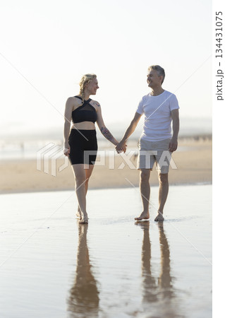 Romantic couple walking on beach holding hands at sunset 134431075