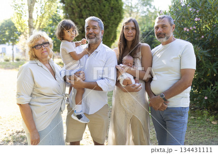 Multi-generational family standing together outdoors enjoying summer day 134431111