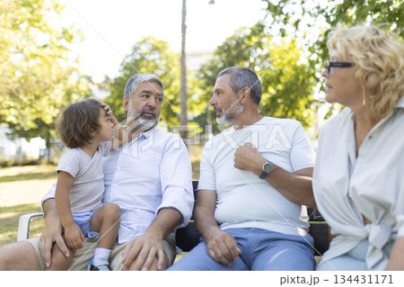 Grandparents and grandchild having conversation sitting on park bench Grandparents and grandchild having conversation sitting on park bench 134431171