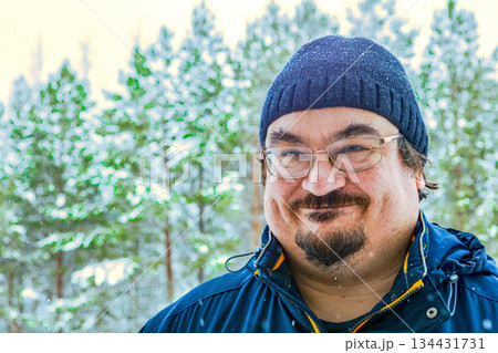 Heavily dressed stocky man trying to hold smile in winter forest closeup Heavily dressed stocky man trying to hold smile in winter forest closeup 134431731