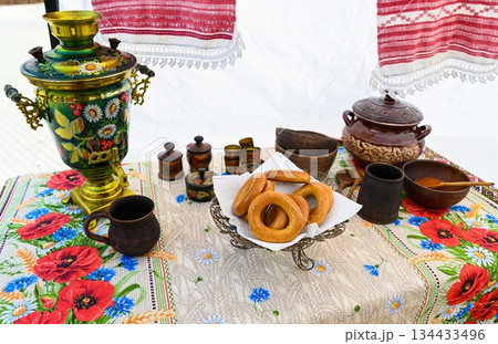 Traditional Slavic tea setting with painted samovar, poppy tablecloth, bagels, and clay dishes. Russian folk culture and colorful patterns. Traditional Slavic tea setting with painted samovar, poppy tablecloth, bagels, and clay dishes. Russian folk culture and colorful patterns. 134433496