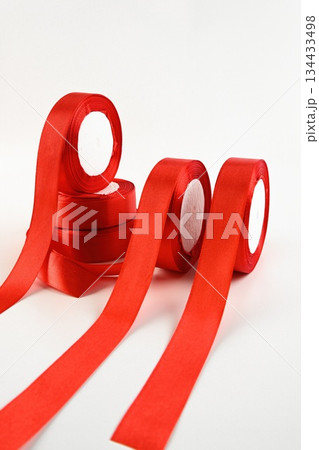 Bright satin ribbons in a vivid red hue arranged in rolls on a clean background. Smooth decorative material ideal for floral design craft gift wrapping and festive projects. Bright satin ribbons in a vivid red hue arranged in rolls on a clean background. Smooth decorative material ideal for floral design craft gift wrapping and festive projects. 134433498