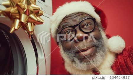 Cheerful man in Santa costume poses next to a washing machine with a festive bow during the holiday season 134434937