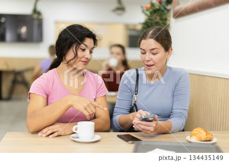 Happy smiling attractive girl emotionally discussing with female friend while dining in restaurant Happy smiling attractive girl emotionally discussing with female friend while dining in restaurant 134435149