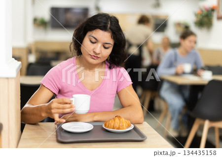 Young woman drinking coffee with croissant in cafe 134435158