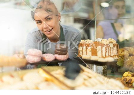 Young woman seller stands at bakery counter, present croissant Young woman seller stands at bakery counter, present croissant 134435187