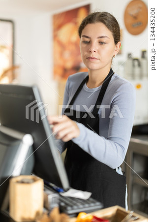Young female cashier at cash register in cafe Young female cashier at cash register in cafe 134435200