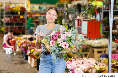 Young woman customer holding bouquet of flowers in open-air plants market 134435308
