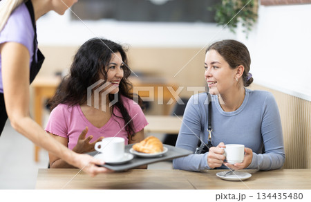 Polite waitress brings coffee and croissant to young girls in cafeteria Polite waitress brings coffee and croissant to young girls in cafeteria 134435480