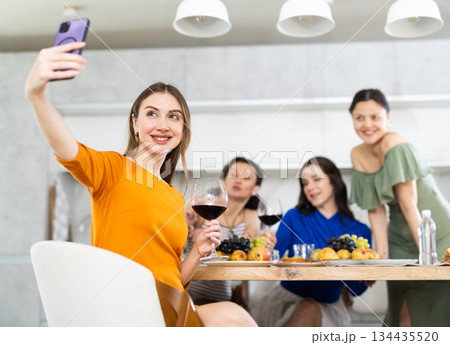 Smiling girl is sitting on chair and taking selfies during gatherings with friends Smiling girl is sitting on chair and taking selfies during gatherings with friends 134435520