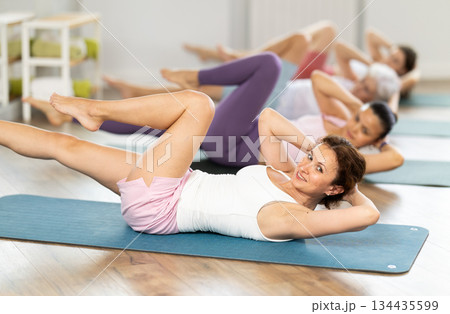 Woman doing elbow to knee crunches during group pilates training Woman doing elbow to knee crunches during group pilates training 134435599