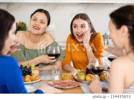 Four women are sitting at table, enjoying food and wine, chatting, talking, laughing. Four women are sitting at table, enjoying food and wine, chatting, talking, laughing. 134435653