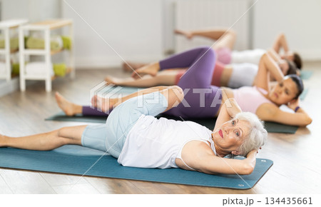 Elderly woman performing supine spinal twist pose at group training 134435661