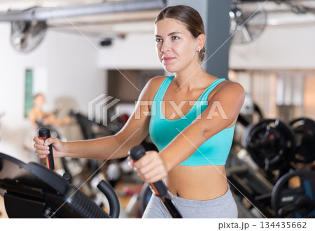 Slender athletic girl during cardio exercises on elliptical simulator in fitness center. Slender athletic girl during cardio exercises on elliptical simulator in fitness center. 134435662