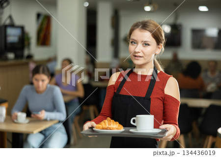 Polite waitress holding tray with coffee and croissant in cafeteria Polite waitress holding tray with coffee and croissant in cafeteria 134436019