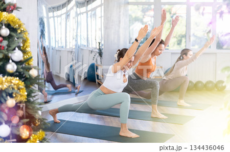 Girl teacher conducts yoga lesson for girls and performs warrior asana in New Year atmosphere. 134436046