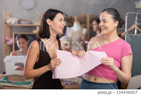 Two young women discuss pattern at sewing master class Two young women discuss pattern at sewing master class 134436057