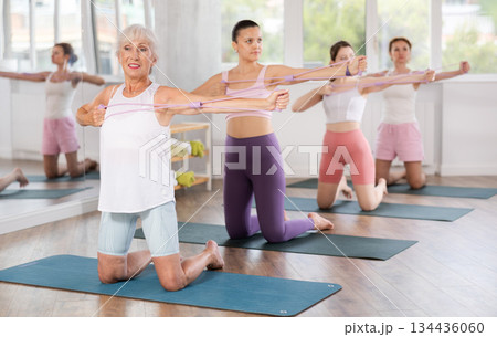 Aged woman exercising with figure eight resistance band in fitness studio 134436060
