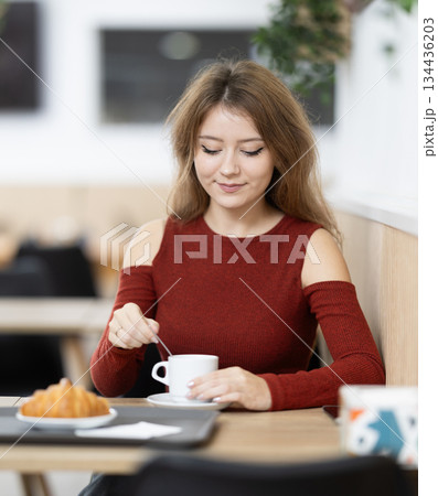 Young female sitting alone at table in cozy cafe, drinking fragrant coffee 134436203