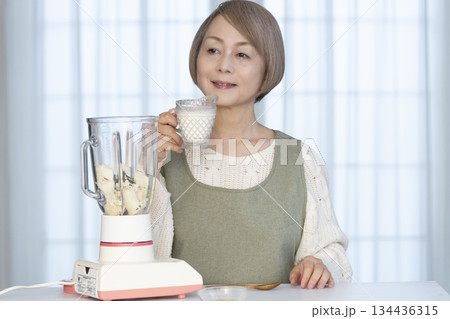 キッチンでヘルシージュースをジューサーで作るシニア女性 134436315