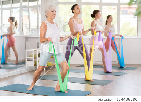 Aged woman exercising with elastic band during group fitness class Aged woman exercising with elastic band during group fitness class 134436380