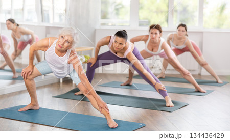 Senior lady performing Side Lunge Pose during group training 134436429