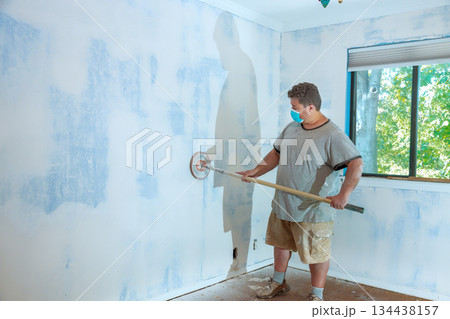 Man works on wall preparation in room with natural light Man works on wall preparation in room with natural light 134438157