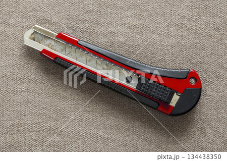 Close-up of isolated stationery retractable metallic knife with sharp blade on light cloth copy space background. Close-up of isolated stationery retractable metallic knife with sharp blade on light cloth copy space background. 134438350