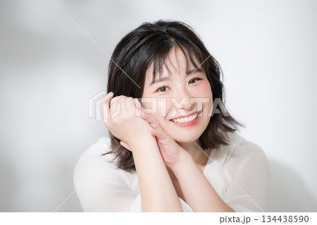 顎に手を当てて(頬杖)笑顔で喜ぶ透明感や多幸感あふれるハッピーな若い癒し系女性の美容イメージクローズ 134438590