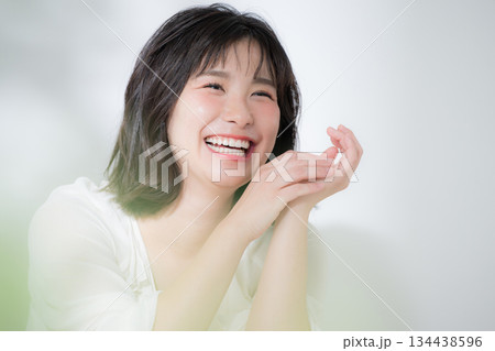 顎に手を当てて(頬杖)笑顔で喜ぶ透明感や多幸感あふれるハッピーな若い癒し系女性の美容イメージクローズ 134438596