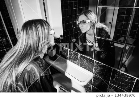 Drunken woman touching her face, looking at her reflection in a bathroom mirror 134439970