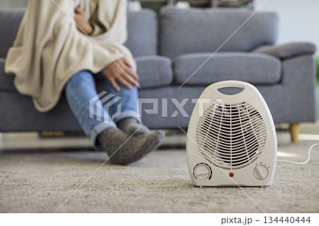 Portable electric heater warms cold living room as man rests under blanket on sofa Portable electric heater warms cold living room as man rests under blanket on sofa 134440444