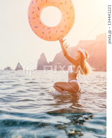 Woman, beach, donut. Happy woman playing with a donut float in the sea at sunset, enjoying summer vacation. 134441221