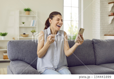 Excited young woman holding phone reading sms with good news or winning online shopping promo 134441899
