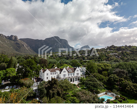 Large white estate with a pool nestled in a lush green valley, surrounded by majestic mountains. Scenic landscape with elegant architecture for travel and luxury brochures. Large white estate with a pool nestled in a lush green valley, surrounded by majestic mountains. Scenic landscape with elegant architecture for travel and luxury brochures. 134443464